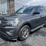 A gray suv parked in the lot of a dealership.